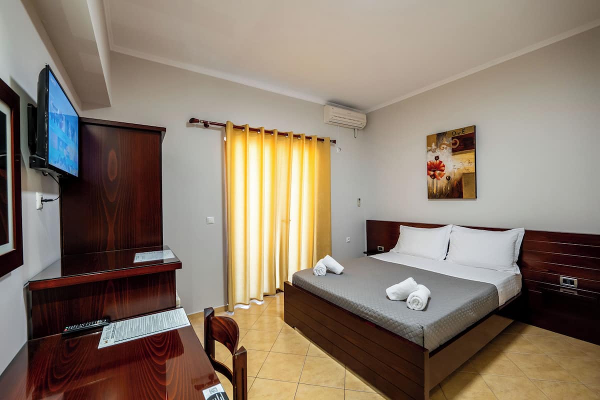 A hotel room with a bed, a desk, a chair, a TV, and a painting on the wall.