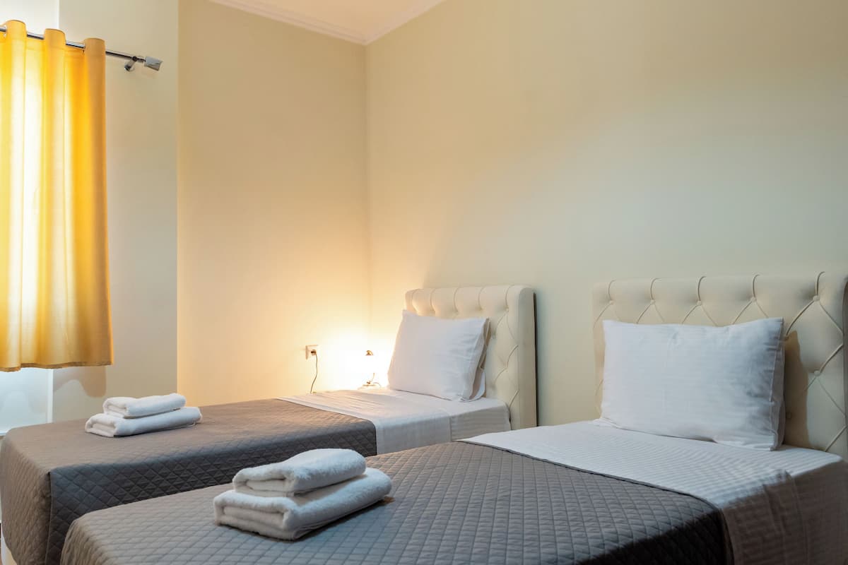 A hotel room with two beds, each with a quilted bedspread and pillows, and a window with yellow curtains.
