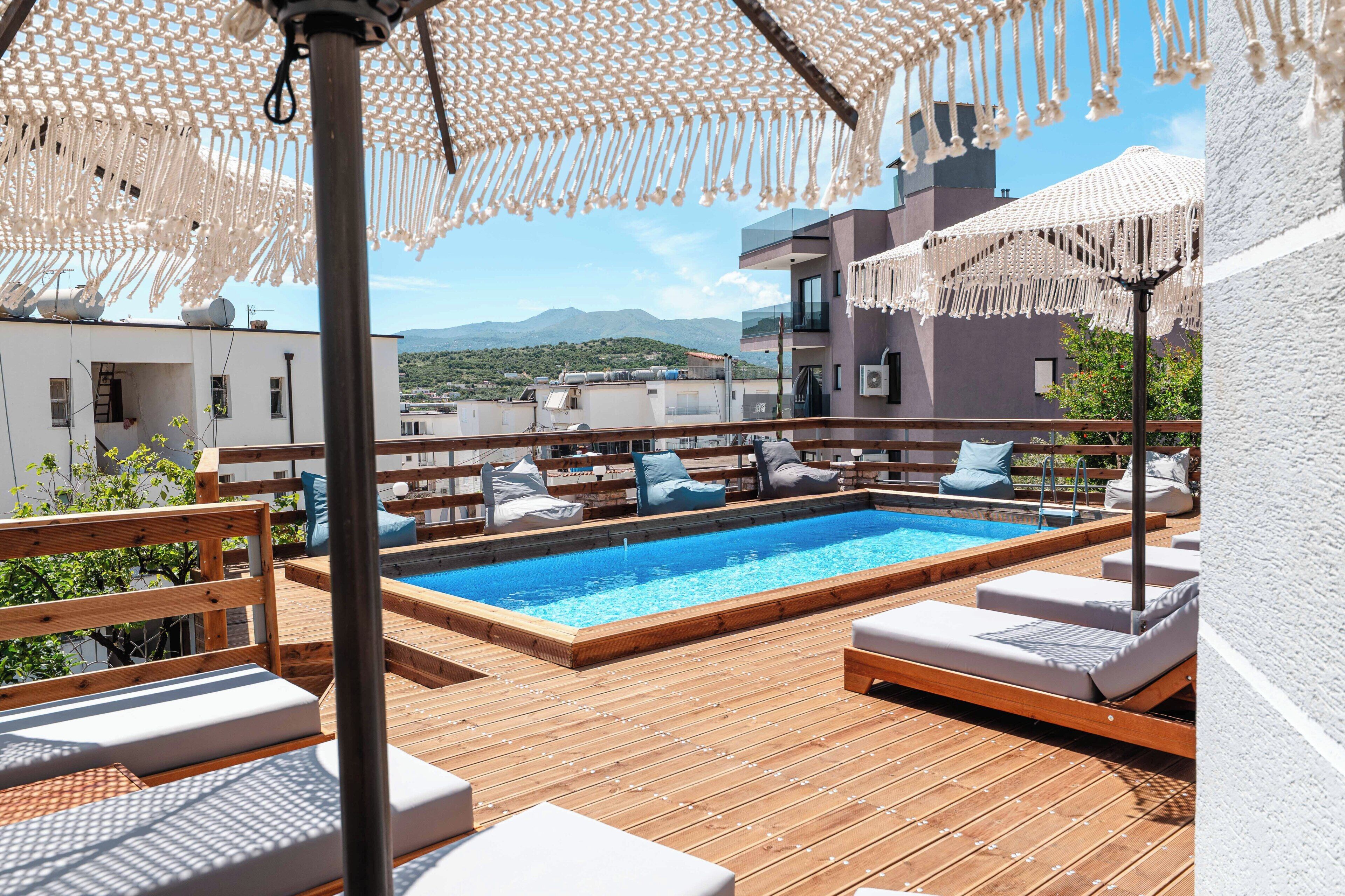 Un espace piscine aménagé sur le toit, avec une terrasse en bois, des chaises longues et une vue sur le paysage urbain.