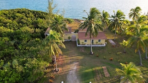 Une propriété située sur la côte, avec une maison jaune, des palmiers et une vue sur la mer.