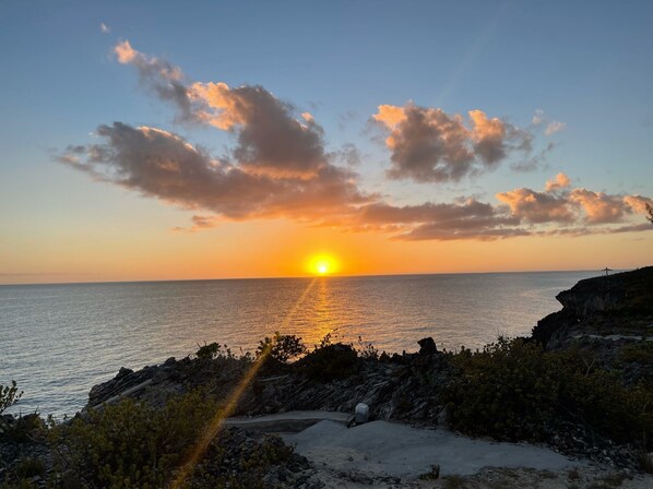 A sunset over a coastal area with rocky terrain and sparse vegetation. - Pineapple Hideaway | Oleander Gardens (Gregory Town)
