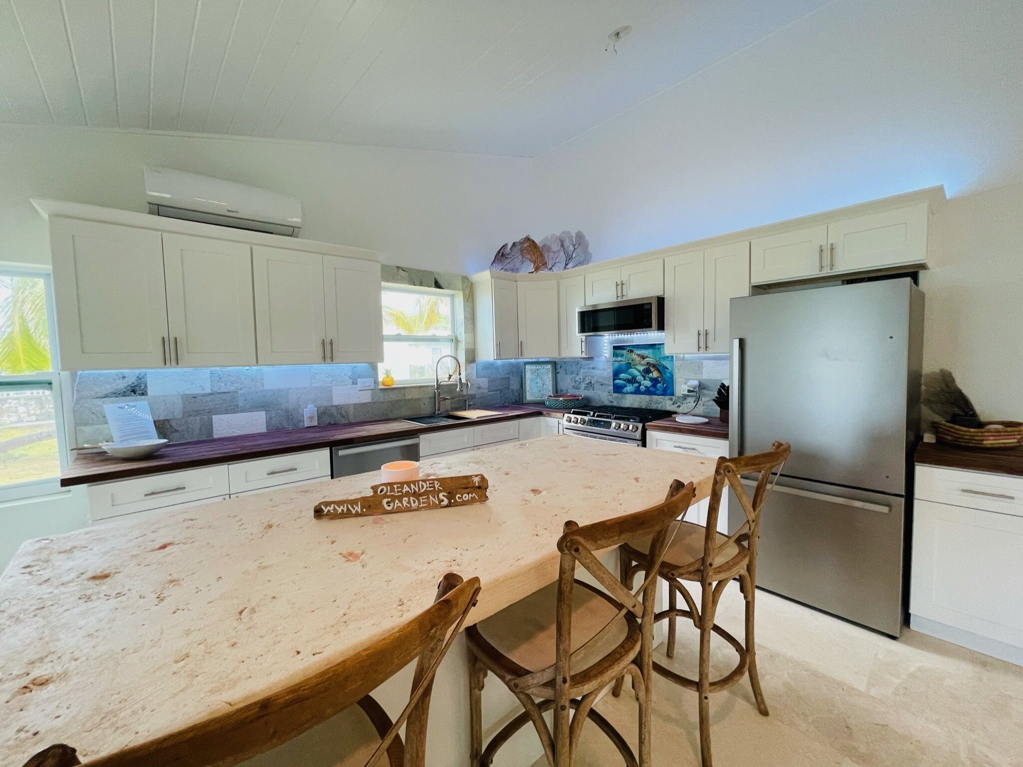 A kitchen with white cabinets, a stainless steel refrigerator, and a wooden island with chairs.