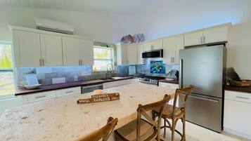 A kitchen with white cabinets, a stainless steel refrigerator, and a wooden island with chairs.