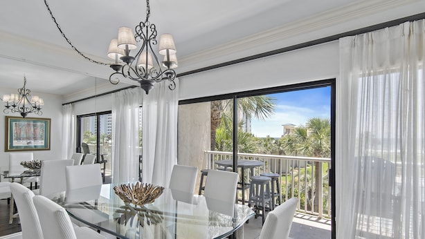A spacious dining area with a glass table and white chairs, a chandelier, and a balcony with outdoor seating. - Gorgeous 3 bedroom 2 bath unit. Beachfront property! (Destin)