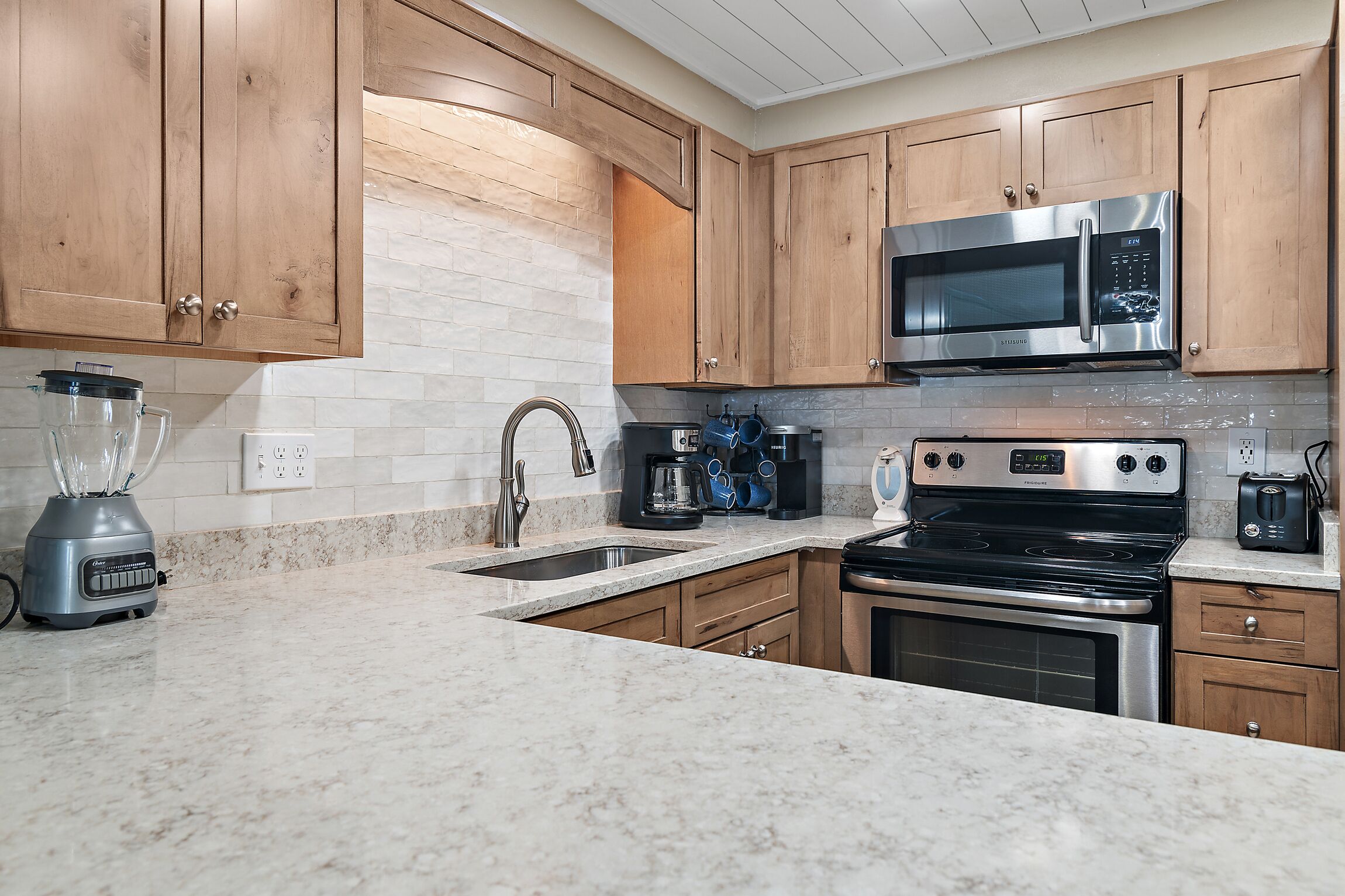 A kitchen with wooden cabinets, a stainless steel microwave, a stove, and a blender.