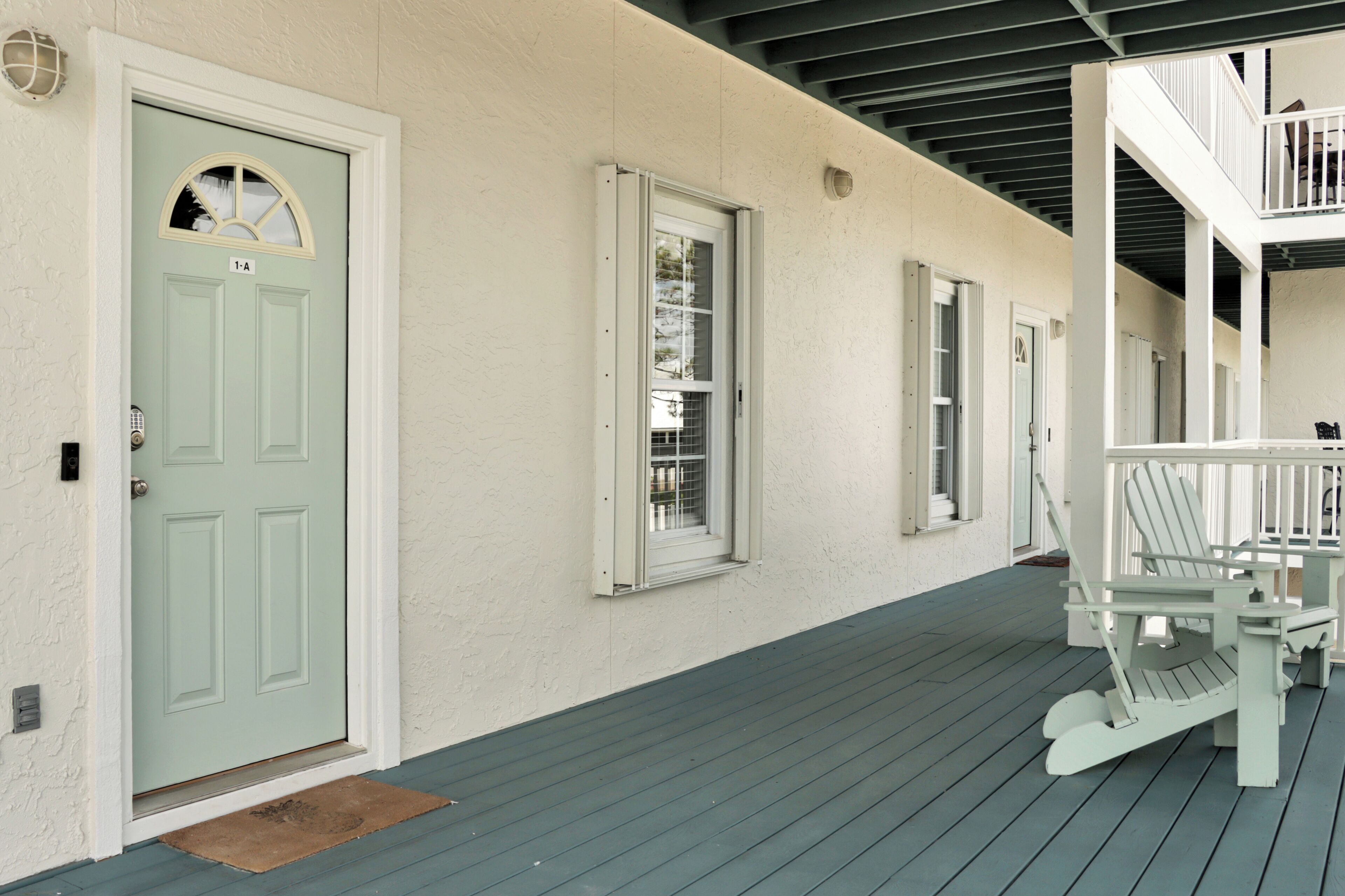 A building with a light green door, white-framed windows, and a wooden deck with two Adirondack chairs.