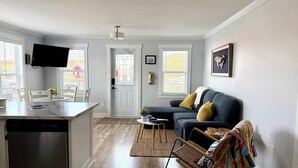 A living room with a sofa, a television, and a dining area with a table and chairs. - Carriage Hill Cottage (Twillingate)
