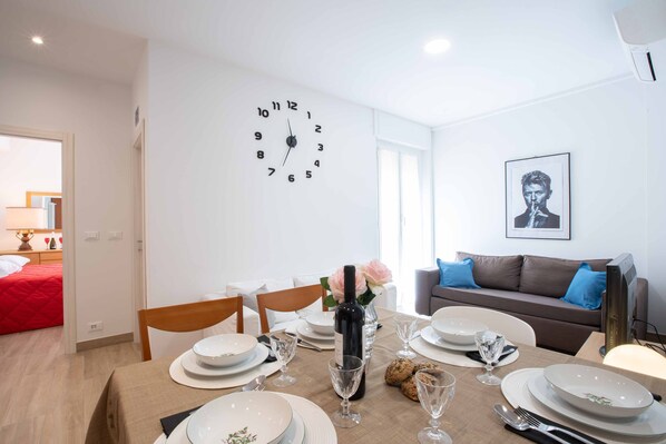 A dining area with a table set for four, a wall clock, and a framed portrait.