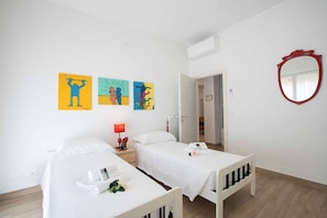 A hotel room with two beds, a red-framed mirror, and three colorful artworks on the wall.