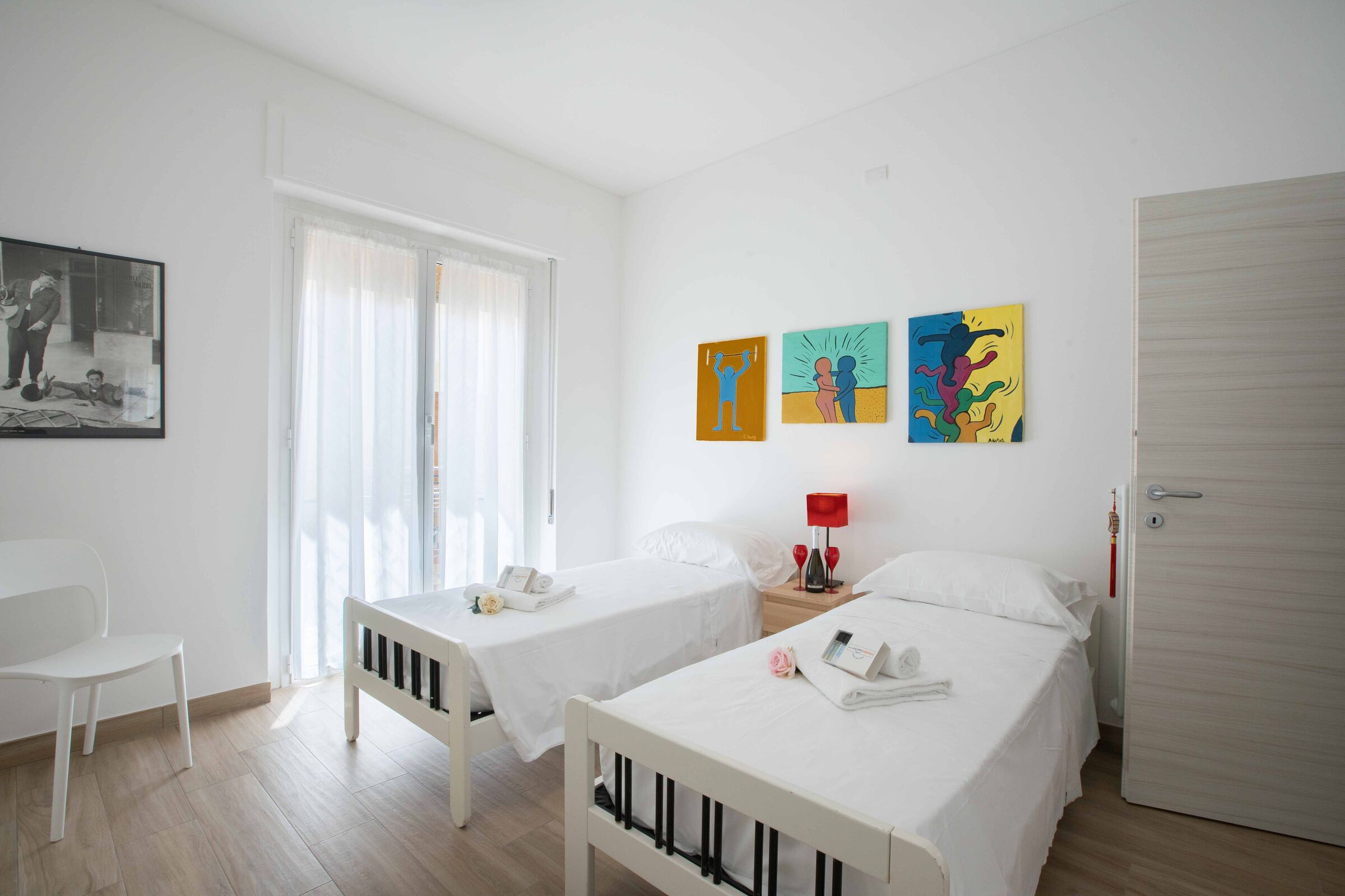 A hotel room with two beds, a chair, a desk, and artwork on the wall.