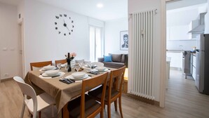 A dining area with a table set for four, a clock on the wall, and a view into the kitchen. - Anne Loren Al Mare (Alassio)