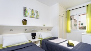 A hotel room with two beds, a white headboard, a small table with a phone and a speaker, a painting on the wall, and a window with yellow curtains. - Home2Book Sun & Pools Costa del Silencio (Costa del Silencio)
