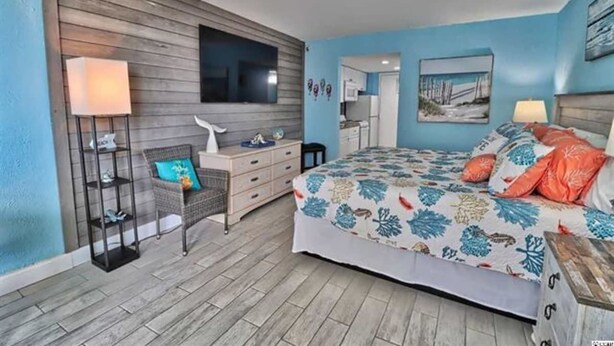 A bedroom with a bed, a dresser, a TV mounted on the wall, and a small kitchenette in the background. - UPDATED UNIT - Beach Getaway Unit 431 (Myrtle Beach)