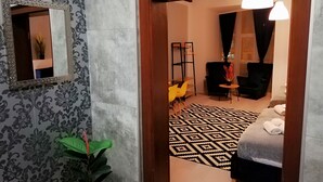 Ein Hotelzimmer mit gemustertem Tapeten, einem Spiegel, einer Pflanze, einem Bett mit gemustertem Teppich und einer Sitzecke mit Stühlen und einem Tisch.