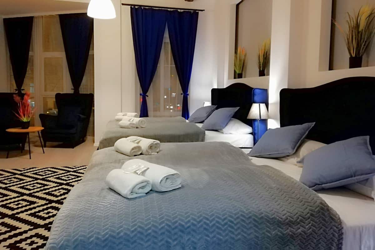 Une chambre d’hôtel avec deux lits, un coin salon comprenant un fauteuil, une petite table et une grande fenêtre avec des rideaux.