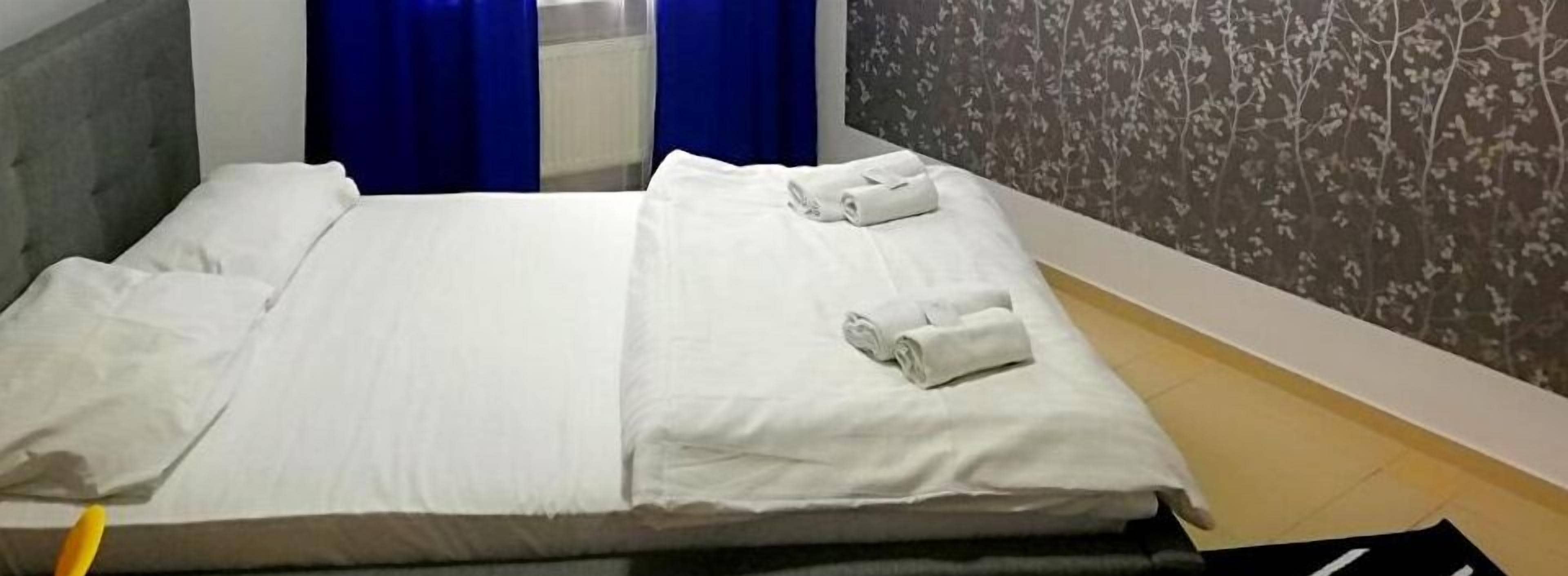 A neatly made bed with white linens and two rolled towels on the side.