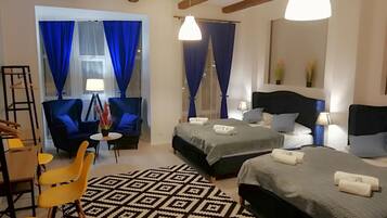 Una camera d'albergo con due letti, un'area pranzo con sedie gialle e un tappeto decorato.
