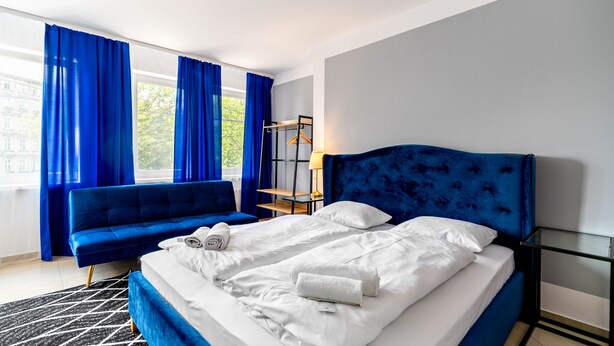 Ein modernes Hotelzimmer mit einem großen Bett, einem blauen Sofa und einem Glastisch.