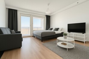 Une chambre d’hôtel moderne équipée d’un lit, d’un canapé, d’une télévision et offrant une vue sur la plage.