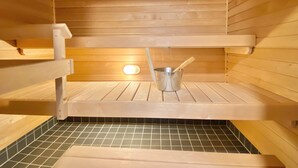 Una sauna con bancos de madera, un cubo metálico y un palo de madera, y un suelo de baldosas.