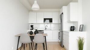Una cocina moderna con armarios blancos, una mesa de comedor de madera, dos sillas, un hervidor negro y una planta en maceta.