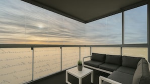 Un balcón moderno con un sofá y una mesita, ventanas amplias con notas escritas a mano y vistas al cielo.