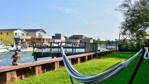 A waterfront area with a grassy walkway, a hammock, and a statue.