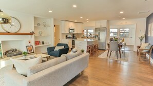 A modern kitchen with white cabinets, a microwave, and a refrigerator. There is a dining area with a table and chairs.