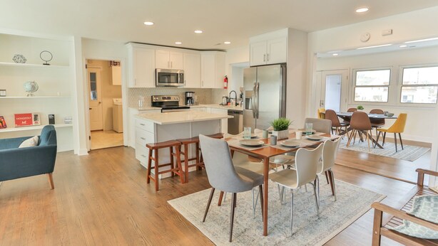 A modern kitchen with white cabinets, a stainless steel refrigerator, and a dining area with wooden chairs and a table.