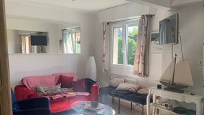 A living room with a red sofa, a glass coffee table, a blue armchair, a small table with a sailboat model, and a window with curtains. - Appartement 8 Personnes, 3mn de la mer , 1 mn de la Thalasso, Centre Ville, (Ouistreham)