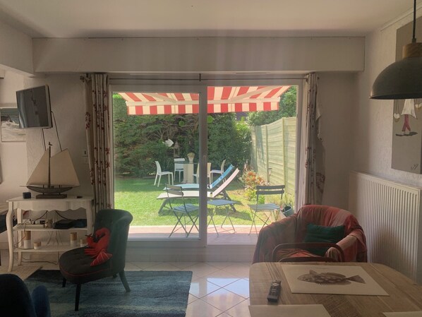 A living room with a sliding glass door leading to a patio with outdoor furniture and a striped awning.