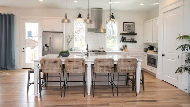 A modern kitchen with a central island, four bar stools, pendant lighting, and a stainless steel refrigerator.
