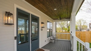 A covered porch with a dark door, two windows, and a wooden ceiling.