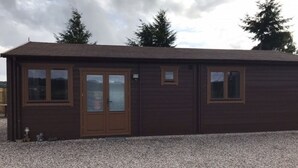 A single-story building with a brown exterior, a front door, and two windows on the side. - Lovely 1-bed House in Fochabers, Scotland (Fochabers)