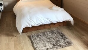 A bedroom with a wooden bed, a fluffy rug, a bedside table, and a hanging light fixture. - Lovely 1-bed House in Fochabers, Scotland (Fochabers)