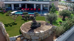 Ein modernes Haus mit Swimmingpool, roten Liegestühlen und gepflegten Gärten.