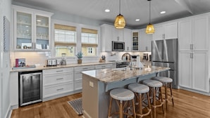 A modern kitchen with white cabinets, a large island with bar stools, stainless steel appliances, and pendant lighting.