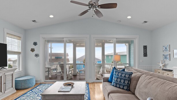 A living room with a ceiling fan, a sofa, a coffee table, and a view through glass doors to an outdoor deck.
