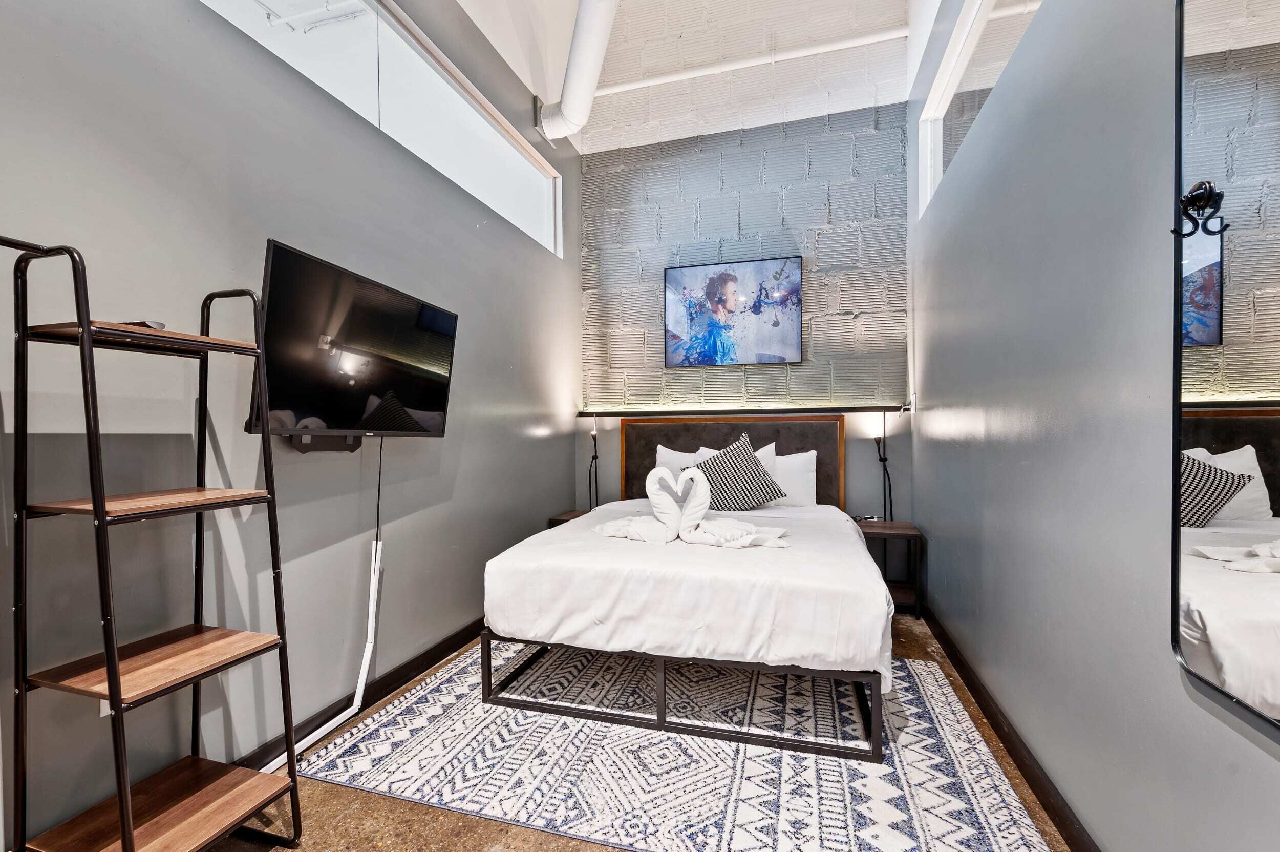 Una habitación de hotel moderna con una cama grande, un televisor montado en la pared, una escalera de madera y una alfombra estampada.