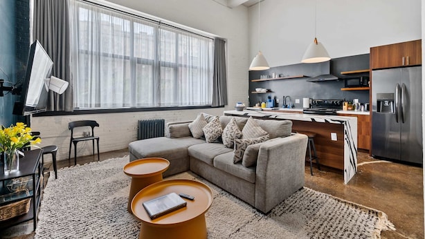 Eine moderne Küche mit großem Fenster, einem grauen Sofa und einem Essbereich mit kleinem Tisch und Stühlen.