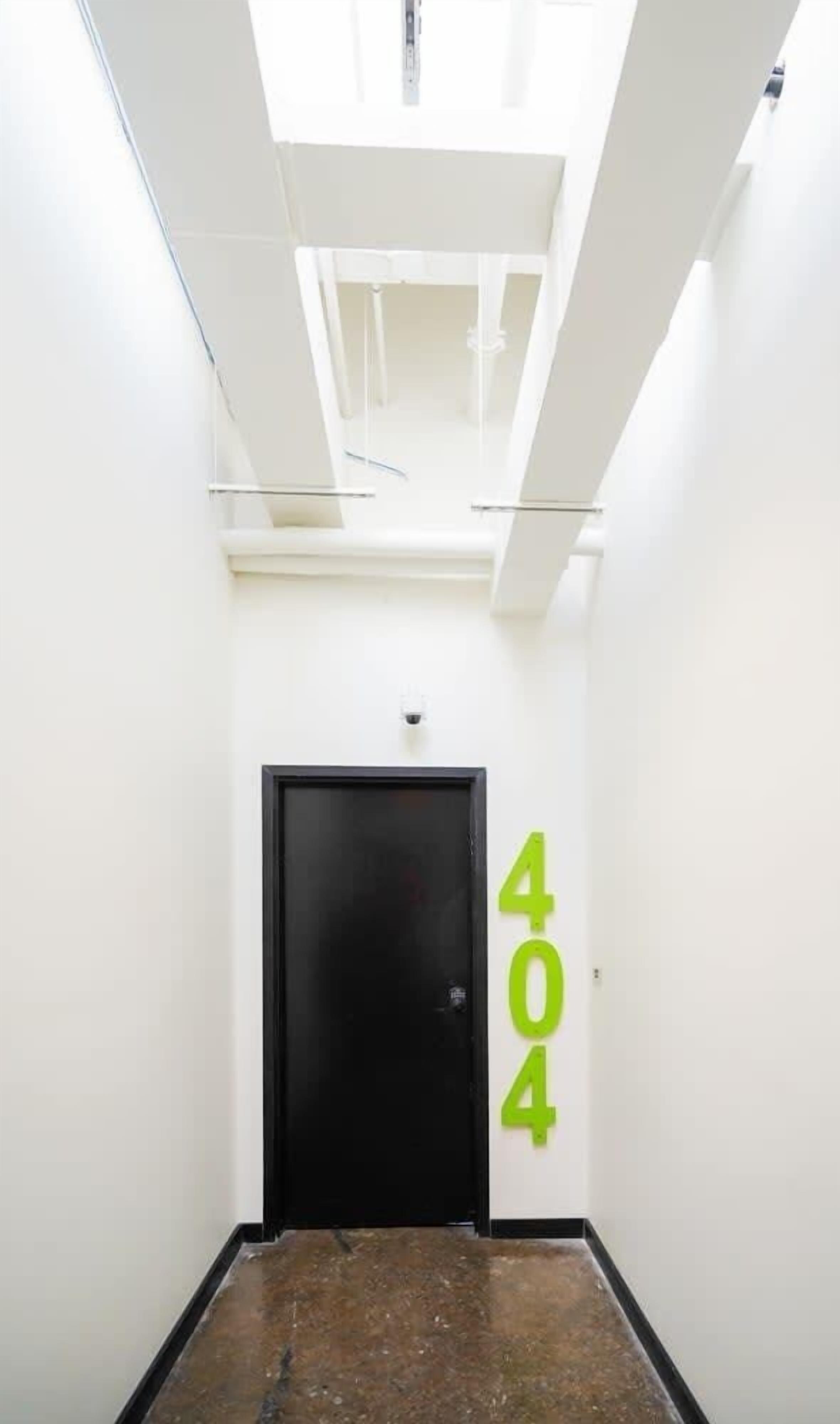 Een smalle gang met een zwarte deur en een groen bordje met het nummer '404' op de muur.