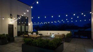 An outdoor patio area with a wooden table and chairs, string lights, and planters.