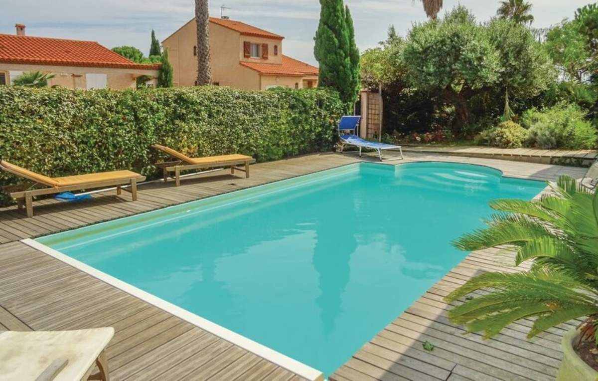 Ein rechteckiger Pool mit Holzterrasse, umgeben von viel Grün und einigen Liegestühlen.