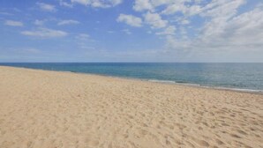 Una playa extensa de arena clara con cielo azul despejado y mar tranquilo.