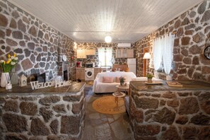 A cozy room with stone walls, a bed, a small kitchen area, and a welcoming 'Welcome Home' sign.