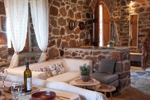 A stone-walled room with a sofa, a small table, and a wine bottle.