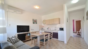 Ein gemütlicher Wohnbereich mit Sofa, Fernseher, Esstisch, Stühlen, Küchenzeile und kleinem Kühlschrank.