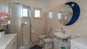 Ein Badezimmer mit Dusche, Toilette, Bidet, Waschbecken und einem großen Spiegel.