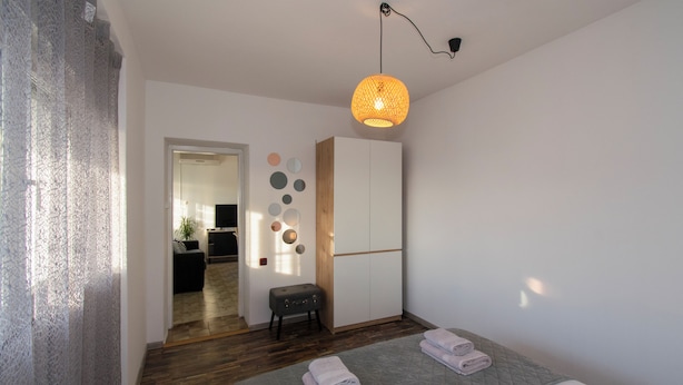 Ein Schlafzimmer mit Bett, Schrank, einem kleinen Hocker und einer Pendelleuchte.