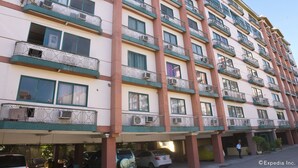 A multi-story hotel with balconies, air conditioning units, and a parking area with cars. - Isabelle Garden Hotel and Suites (Parañaque)
